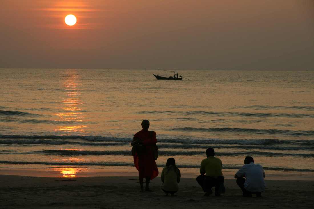 A Buddhist monks blesses tourists on a beach in Thailand